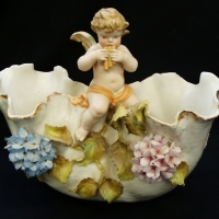 A VICTORIAN figural porcelain vase with applied finely detailed hydrangeas leaves & a cherub playing a pan flute Crossed blue sword marks to base - af - Sold for $37 - 2015
